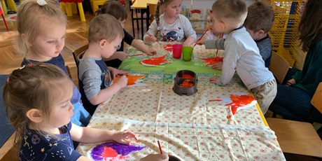Powiększ grafikę: Dzieci siedzą przy stole. Malują farbami