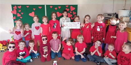 Powiększ grafikę: Grupa dzieci ubrana na czerwono pozuje do zdjęcia. Dwie dziewczynki trzymają kartkę z napisem "Walentynki"