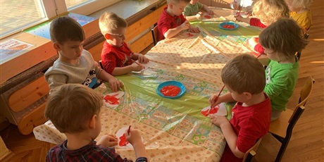 Powiększ grafikę: Dzieci siedzą przy stole. Malują czerwoną farbą