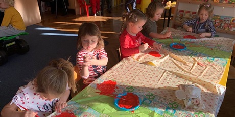 Powiększ grafikę: Dzieci siedzą przy stole. Malują czerwoną farbą