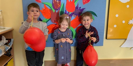 Powiększ grafikę: Dwóch chłopców trzyma czerwone balony w kształcie serca. Pomiędzy nimi stoi dziewczynka