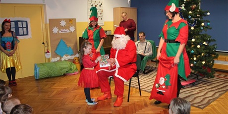 Powiększ grafikę: Do mężczyzny przebranego za Świętego Mikołaja podchodzi dziewczynka z prezentem