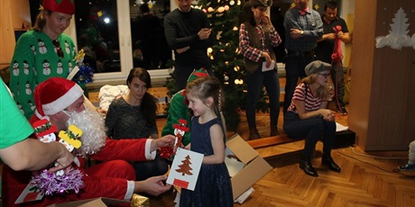 Powiększ grafikę: Dziewczynka podchodzi do mężczyzny przebranego za Mikołają i wręcza mu prezenty
