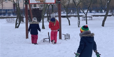 Powiększ grafikę: Zima.Trójka dzieci ubrana w kurtki stoi w przedszkolnym ogrodzie