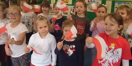 Powiększ grafikę: Dzieci machają flagami Polski. Po prawej stronie dziewczynka ubrana jest w koszulkę z orłem białym