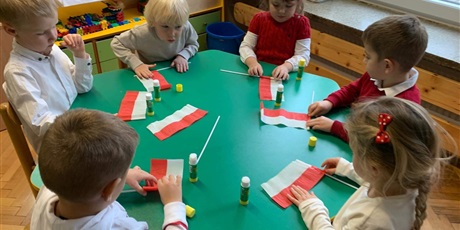 Powiększ grafikę: Dzieci siedzą przy stole. Robią flagi Polski