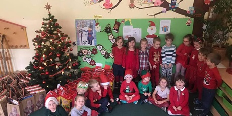 Powiększ grafikę: Grupa dzieci ubrana czerwono pozuje do zdjęcia. Obok nich stoi choinka z prezentami