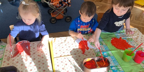 Powiększ grafikę: Trójka dzieci siedzi przy stole. Malują czerwoną farbą