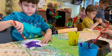 Powiększ grafikę: Zbliżenie na chłopca. Dzieci malują farbami. W tle dzieci bawią się klockami