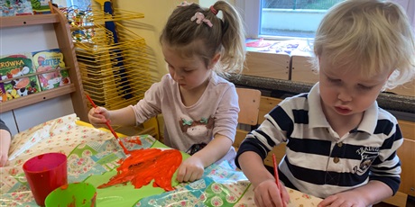 Powiększ grafikę: Dziewczynka i chłopiec siedzą przy stole. Malują farbami