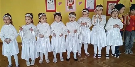 Powiększ grafikę: Osiem dziewczynek w białych strojach. Obok nich stoi dwójka chłopców przebrana za skrzaty