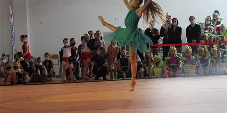 Powiększ grafikę: Dziewczynka w niebieskiej sukience pokazuje figurę taneczną. W tle przebrane grupy taneczne oraz dorosłe osoby  w maskach