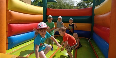 Powiększ grafikę: Dzieci skaczą na pompowanej trampolinie. Uśmiechają się
