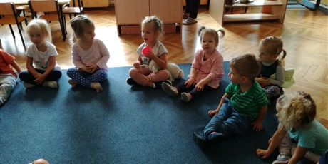 Powiększ grafikę: Dzieci siedzą na dywanie. Dziewczynka trzyma w ręku różową piłkę