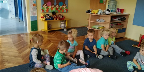 Powiększ grafikę: Dzieci siedzą na dywanie. Siedzą do siebie odwrócone wzajemnie