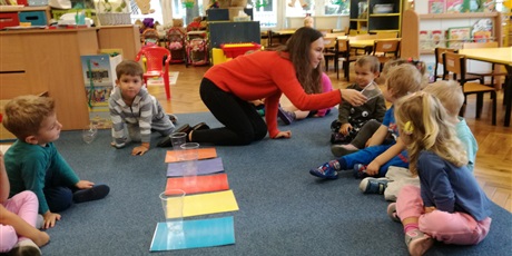 Powiększ grafikę: Nauczycielka podczas zajęć na dywanie podaje kubek dziecku