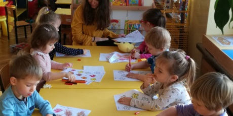 Powiększ grafikę: Dzieci siedzą przy stolikach. Kolorują karty pracy
