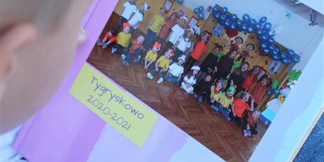 Powiększ grafikę: Dziecko patrzy na kronikę przedszkolną, w której jest przyklejone zdjęcie z podpisem "Tygryskowo 2020-2021"