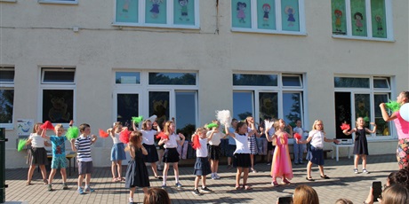 Powiększ grafikę: Dzieci stoją w dużej grupie na podwórku przedszkolnym, tańczą z kolorowymi pomponami