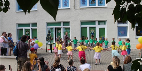 Powiększ grafikę: Grupa dzieci w żółtych i zielonych koszulkach stoi wraz z nauczycielką w dużym kole