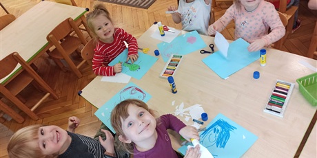 Powiększ grafikę: Dzieci wykonują pracę plastyczną przy stole. Uśmiechają się